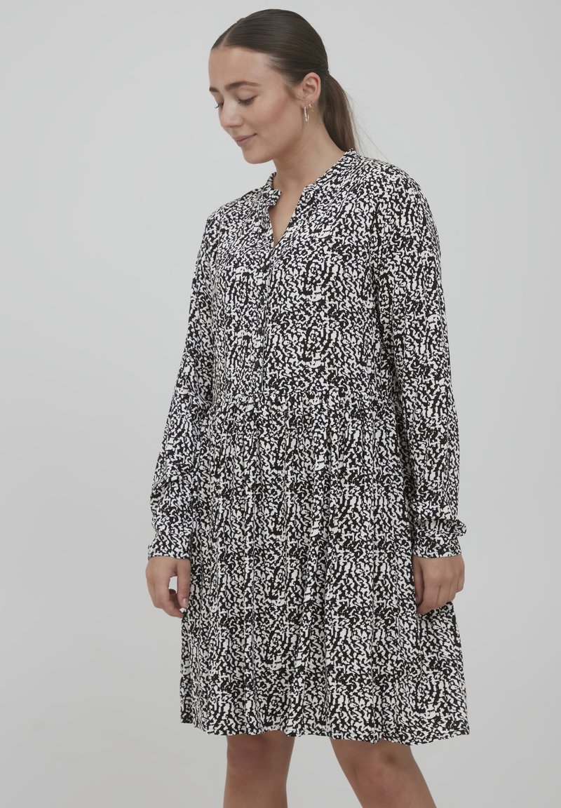 Schwarz-weißes Kleid mit lässiger Passform, das ein strukturiertes Muster, lange Ärmel und einen Knopfverschluss am Ausschnitt aufweist.