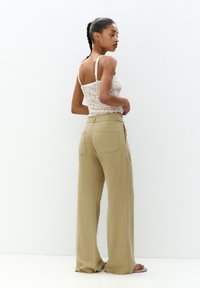 Lichtbeige linnen broek met wijde pijpen, gecombineerd met een aansluitend crèmekleurig kanten top. De outfit heeft dunne bandjes en een gestructureerde afwerking.