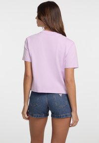 Violets kokvilnas T-krekls ar īsām piedurknēm un saīsinātu dizainu, savienots ar džinsu šortiem ar salocītām malām un nelielu logo birku aizmugurē.