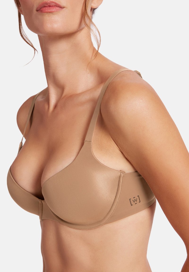 Lätt, sömlös bh i tan tyg. Har justerbara axelband, en formar kupa design och subtil branding på sidan. Slät textur.