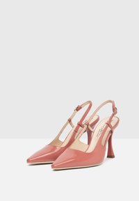 Różowe lakierowane szpilki typu slingback z pointed toes i obcasem stiletto. Posiadają regulowany pasek w okolicy kostki oraz wycięcia po bokach.