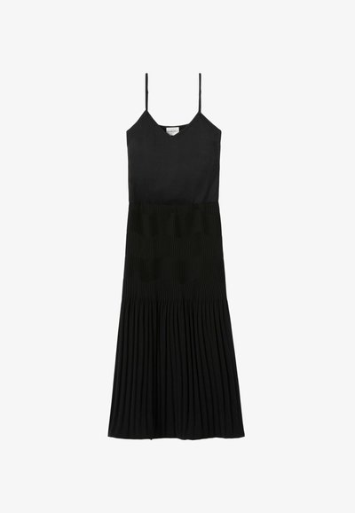 Abito nero con sottili spalline, corpetto aderente e gonna plissettata. Realizzato in tessuto liscio con una sezione inferiore strutturata.