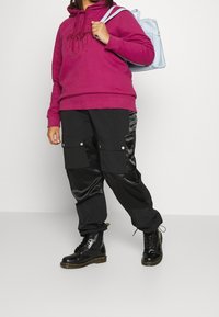 Fuksjowy hoodie z graficznym nadrukiem, zestawiony z czarnymi spodniami cargo z błyszczącymi elementami i dużymi kieszeniami. Czorne botki dopełniają stylizację.