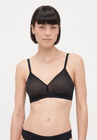 Must mustriga rinnahoidja, mis on valmistatud läbipaistvast kangast, millel on kolmnurksed cup'id, kitsad reguleeritavad rihmad ja lai alläär õrna äärisega.