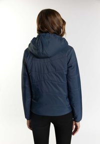 Giacca puffer blu navy con cappuccio, caratterizzata da una texture trapuntata e una silhouette aderente. Polsini e orlo elasticizzati, branding minimale visibile.