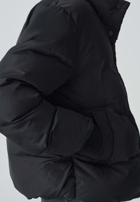 Giacca a vento nera con finitura lucida, caratterizzata da un colletto alto, tasche laterali e dettagli a coste sui polsini.