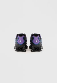 Black athletic shoes with a textured surface, featuring purple and blue accents, a rounded heel, and distinctive black cushioned soles.