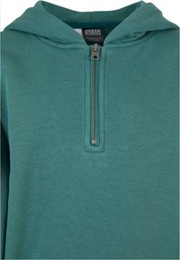 Zelená mikina na zip vyrobená z měkké látky s polo-zip uzávěrem, která má kapuci a žebrované detaily kolem výstřihu a manžet.