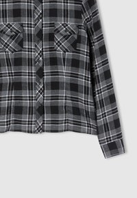 Camicia in flanella a quadri neri e grigi con maniche lunghe, due tasche sul petto, chiusura con bottoni e una texture morbida.