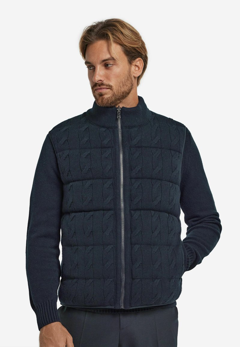 Granatowa kamizelka zapinana na zamek, z wzorem warkocza na górze, prążkowanymi mankietami i kołnierzem, połączona z gładką fakturą reszty materiału.