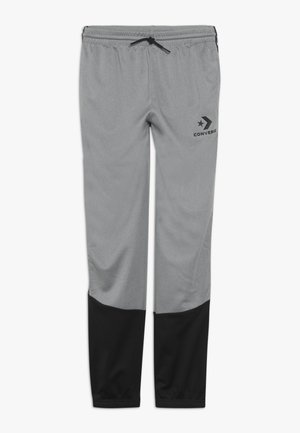 Pantalon de jogging gris et noir avec taille élastique et cordon noir, avec un logo Converse noir sur la partie supérieure de la jambe gauche.