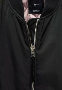 Schwarze Bomberjacke mit glattem Außenmaterial, ausgestattet mit einem silbernen Reißverschluss und einem gerippten Kragen. Innen ist ein hellrosa Futter sichtbar.