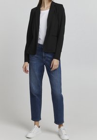 Černý blazer přes bílý tričko, v kombinaci s modrými přímými džínami a bílými teniskami. Hladká tkanina, přiléhavý střih a uvolněná silueta.