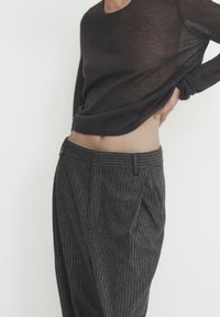 Person wearing a dark brown long sleeve top and gray pinstripe pants, with one hand resting on their back and midriff exposed.