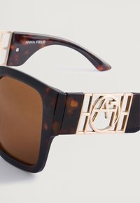 Γυαλιά ηλίου με σκούρα καβούρια, καφέ φακούς, χρυσές λεπτομέρειες με λογότυπο και παχιές γεωμετρικές βραχίονες. Διαθέτουν χαρακτικά λογότυπα στις βραχίονες.