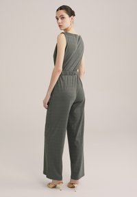Šedý, bezramenný overal s volným střihem, elastickým pasem a širokými nohavicemi zobrazený ze zadní strany. Hladká textura, minimalistický design.