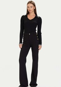 Czarna prążkowana bluzka z długim rękawem i dekoltem w serek oraz biały kołnierzyk w paski, zestawiona z czarnymi spodniami z wysokim stanem ozdobionymi guzikami.