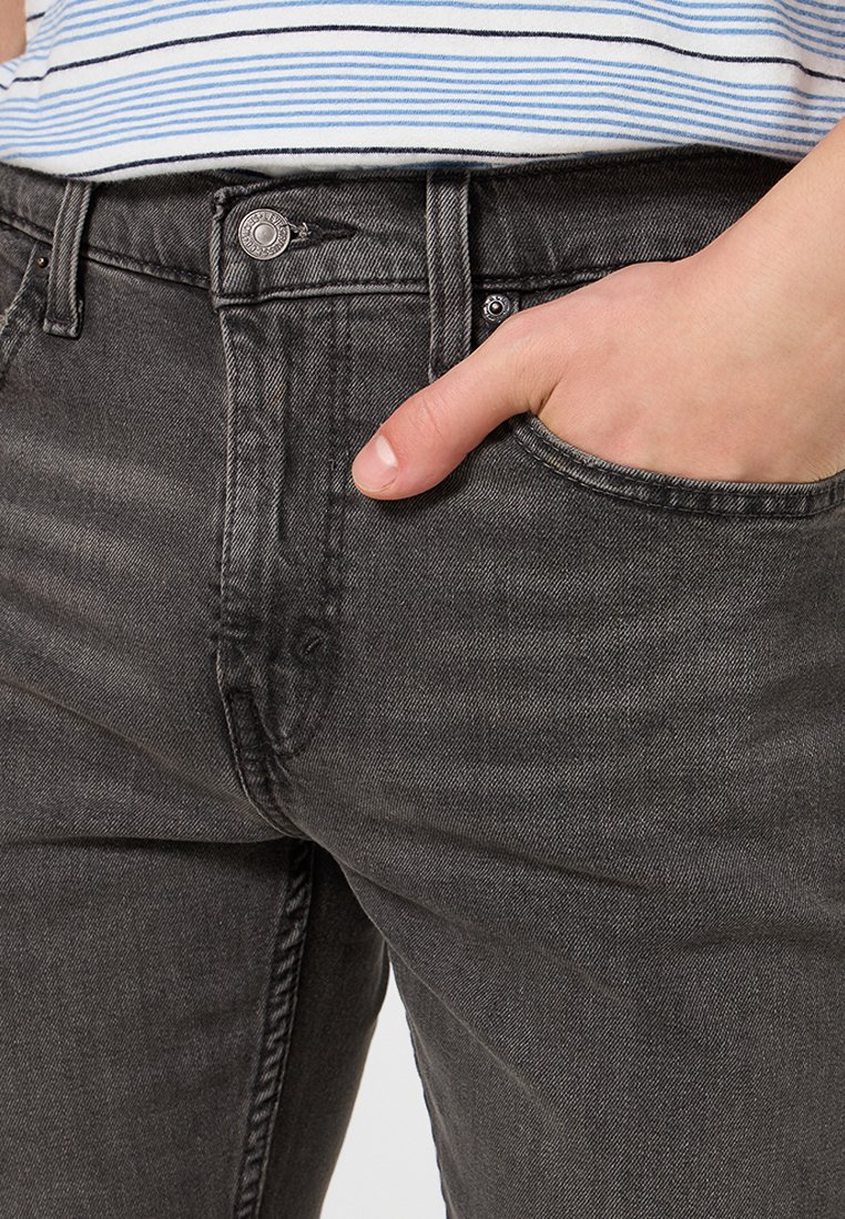 Schwarze Jeans aus Denim mitSlim-Fit, ausgestattet mit einer Fronttasche, sichtbaren Nähten und einem Metallknopfdetail in der Taille.