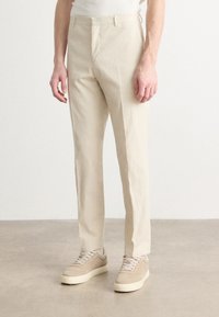 Lichtbeige op maat gemaakte broek van een geweven stof, met een recht gesneden ontwerp en voorzakken. Gecombineerd met beige sneakers.