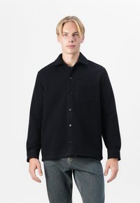 Navy blue, textured fleece jacket with a collared neck, button closure, and single chest pocket, paired with light wash jeans.