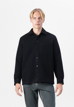 Navy blue, textured fleece jacket with a collared neck, button closure, and single chest pocket, paired with light wash jeans.