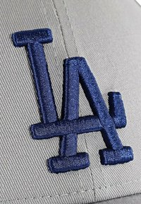 Cappellino da baseball grigio con logo "LA" ricamato in blu navy scuro. Il design include cuciture in rilievo per texture e profondità.