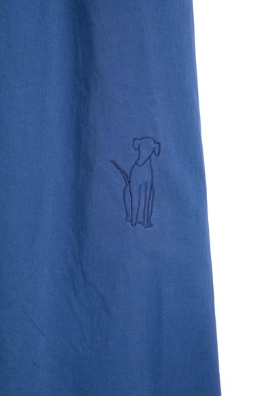 Tissu bleu avec un contour simple cousu représentant un chien assis en fil foncé près du centre.