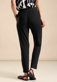 Pantalones negros ajustados con una textura suave, con una cintura de media altura y dos bolsillos traseros. Llevados con sandalias de malla negras.