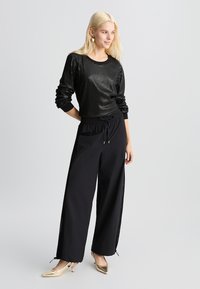 Sweatshirt nero con paillettes, maniche lunghe, abbinato a pantaloni neri a taglio comodo con cerniere laterali e décolleté oro a punta.
