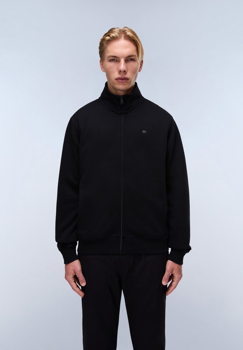 Černá mikina na zip s vysokým límcem, obsahující malé logo na hrudi a žebrované manžety a spodní lem. Materiál vypadá měkce a má texturovaný povrch.