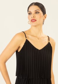 Vestido negro plisado con escote en V, tirantes finos y detalles en tono dorado en los hombros. Tela ligera con un diseño fluido.