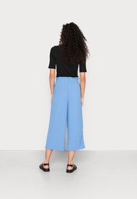 Blå vida byxor med elastisk midja, tillverkade av mjuk tyg. Kombinerat med en svart kortärmad topp och svarta sandaler.