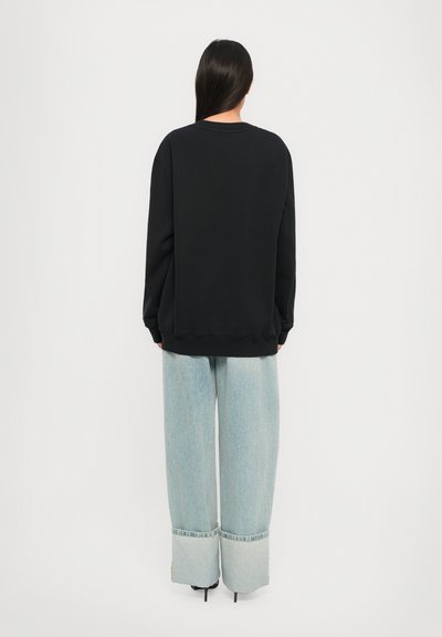 Sudadera negra con un ajuste holgado, puños y dobladillo acanalados. Combinada con jeans de pierna ancha de color azul claro con dobladillos remangados y bordes deshilachados.