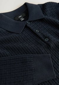 Marineblaue Strick-Polohemd mit einem strukturierten, quadratischen Muster. Verfügt über einen Kragen und drei schwarze Knöpfe auf der Vorderseite. Weiches Material.