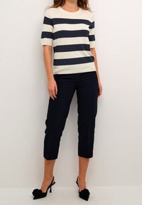 Gestreifter Kurzarmpullover in Marineblau und Creme, kombiniert mit marineblauen, cropped Hosen; schwarze Slingback-Absätze mit rosafarbenem Akzent. Weiche Textur, lässige Passform.