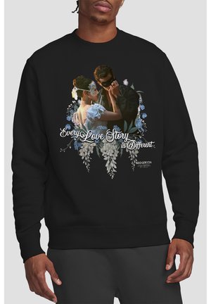 Man wearing black sweatshirt featuring a masked couple embracing with floral accents and text "Every Love Story is Different."
