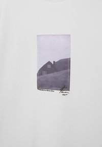 Photo en noir et blanc d'une maison sur une colline imprimée sur un tissu blanc avec le texte "Photographie par Gloria Silva" en dessous.