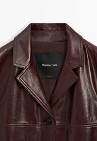 Giacca in pelle bordeaux con colletto appuntito, chiusura a un bottone nero e etichetta nera con il testo "Massimo Dutti".