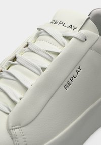 Άσπρα δερμάτινα αθλητικά παπούτσια με λεία υφή, με λευκά κορδόνια, στρογγυλεμένη μύτη και λογότυπο "REPLAY" στο πλάι και στη γλώσσα.