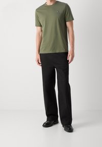 Camiseta de algodón verde oliva con mangas cortas y cuello redondo, con un pequeño logotipo en el pecho, combinada con pantalones negros de pierna recta.