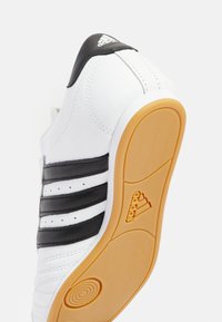 Vita sneakers med svarta ränder, slätt syntetiskt material, rund tå, gummisulor med ett strukturerat mönster och Adidas-logotyp på hälen.