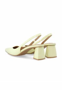 Keltainen patenttinahkainen slingback-kengät, joissa on leikkauksen muotoilu, neliskanttiset korot ja teksturoitu ruskea sisäpohja. Ominaisuutena matala kulma selkäosassa.