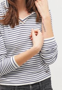 Donna che indossa una maglietta a righe bianche e blu con maniche lunghe mostra un tatuaggio di numeri romani sul braccio interno.