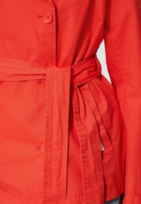 Sarkans uzvalks ar jostu viduklī, diviem pogām un sānu kabatām. Izgatavots no kokvilnas ar gludu tekstūru un tīru dizainu.