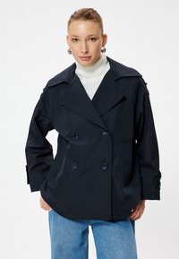 Giacca doppiopetto blu navy con collare a rever, dettagli con bottoni sulle maniche, due tasche e una vestibilità rilassata, abbinata a un dolcevita bianco.