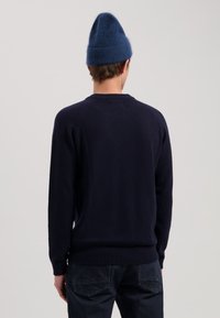 Marineblauwe wollen trui met een ronde halslijn, geribbelde manchetten en zoom. G gedragen met donkere jeans en een blauwe gebreide muts. Effen gestructureerde stof.