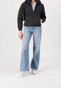 Czarna kurtka puchowa z zamkiem z przodu i kapturem, w połączeniu z jasnoniebieskimi spodniami o szerokich nogawkach i białymi trampkami. Minimalistyczna czarna torebka na ramieniu.