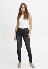 Fekete, skinny farmernadrág magas derékkal, elülső zsebekkel és kopott hatású acabálással. Fehér ujjatlan top és szürke, hegyes orrú magassarkúk kíséretében.