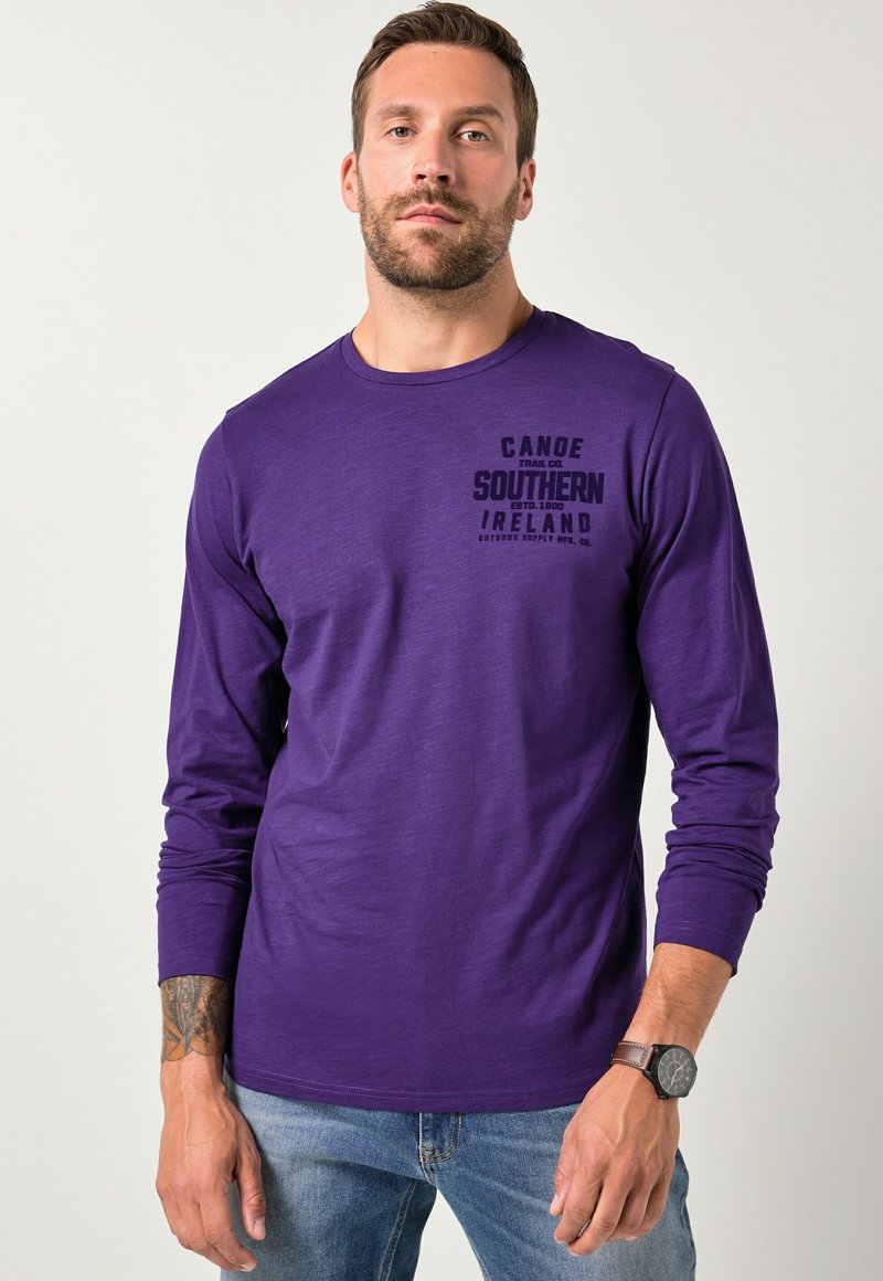 Lila langärmliges T-Shirt mit Rundhalsausschnitt, ausgestattet mit einem schwarzen Druck "Canoe Southern Ireland" auf der linken Brust. Weicher Stoff.