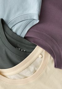 Fire T-shirts i lyseblå, mørkegrøn, beige og bordeaux stablet sammen, med rund halsudskæring og tekstur af bomuldsstof.